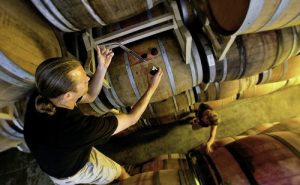 man tasting red wine from a barrel