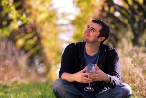 Gary Vayberchuk holding a glass of wine sitting in a field looking up